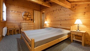 A wooden cabin bedroom with a bed, dresser, and two bedside lamps.