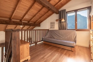 Un dormitorio estilo loft acogedor, con techo de madera, un ventanal con vistas a la montaña, un banco de madera y una mesita.