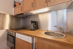 Una cocina compacta con armarios de madera, un lavamanos de acero inoxidable, una cafetera y un lavavajillas.