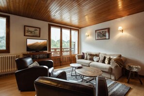 A cozy living room with a wooden ceiling, a sofa, a coffee table, and a television.