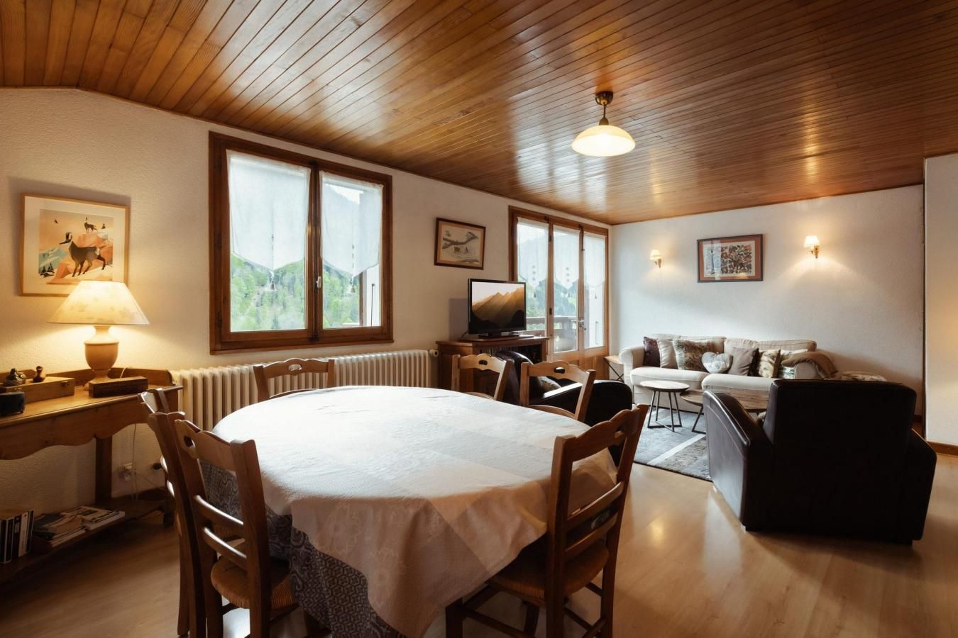 A cozy room with a wooden ceiling, a dining table with chairs, a sofa, and a television.