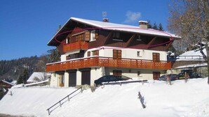 A two-story chalet with a wooden balcony and a ski lift in the background.
