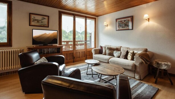 A cozy living room with a wooden ceiling, a sofa, a coffee table, and a television.