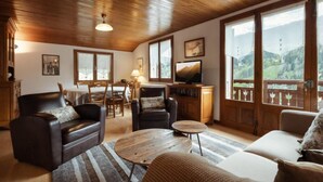 A cozy living room with wooden ceiling, a television, and large windows offering a mountain view.
