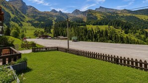 A rural road with a wooden fence, a building with a sloped roof, and mountains in the background.