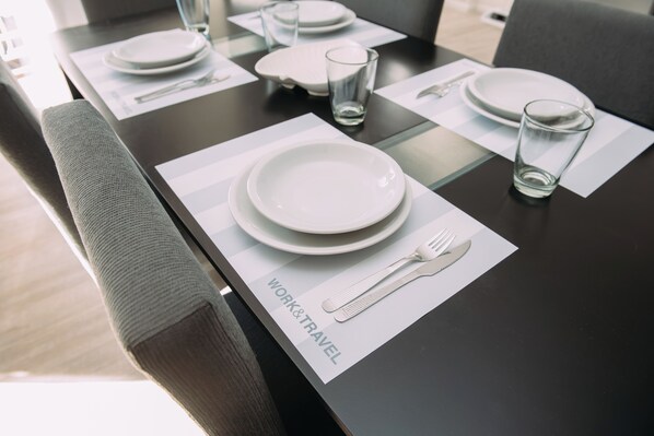 A dining table set for a meal, featuring white plates, clear glasses, and cutlery, including a fork and knife, on a dark table surface with a placemat.