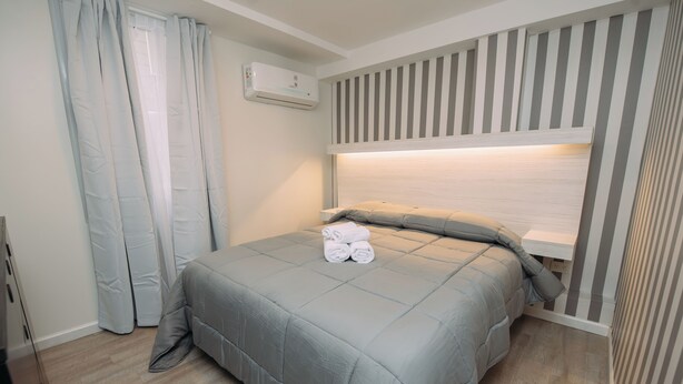 A neatly made bed with a grey duvet and pillows, a white air conditioning unit on the wall, and a striped headboard. - Maison Work & Travel 1 - Palermo (Buenos Aires)