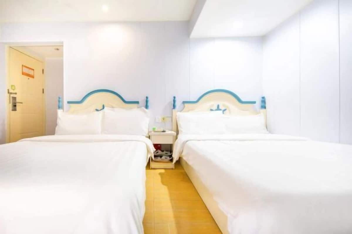 Une chambre d’hôtel avec deux lits simples, un plancher en bois et une porte blanche.