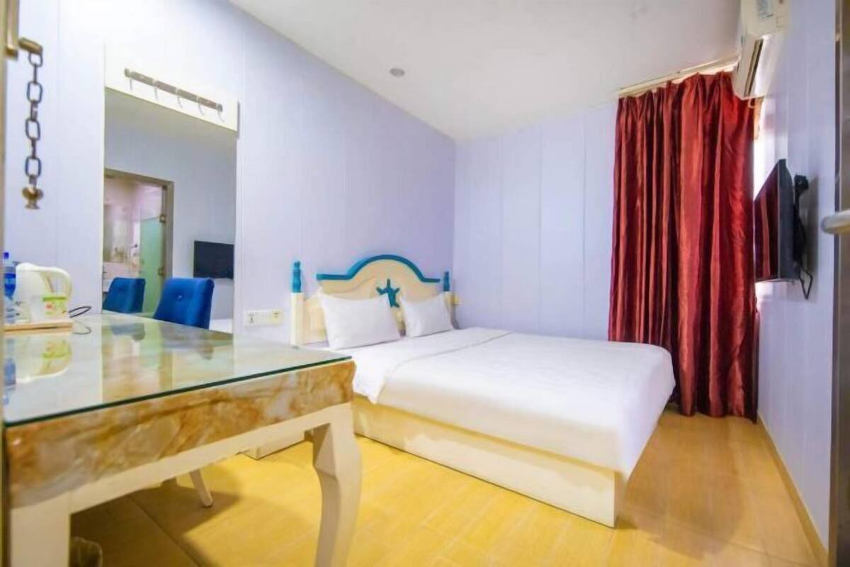 Une chambre d’hôtel avec un lit, une table en verre, une chaise, un téléviseur et un rideau rouge.