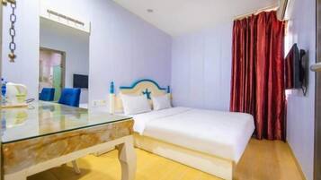 A hotel room with a bed, a glass table, a chair, a TV, and a red curtain.