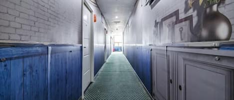 A corridor with a patterned floor, doors on the left, and a wall with a vase and flowers on the right.