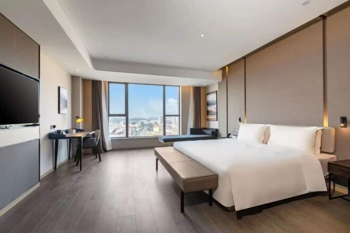 Une chambre d’hôtel moderne équipée d’un grand lit, d’un bureau, d’une chaise, d’un banc et d’un téléviseur.