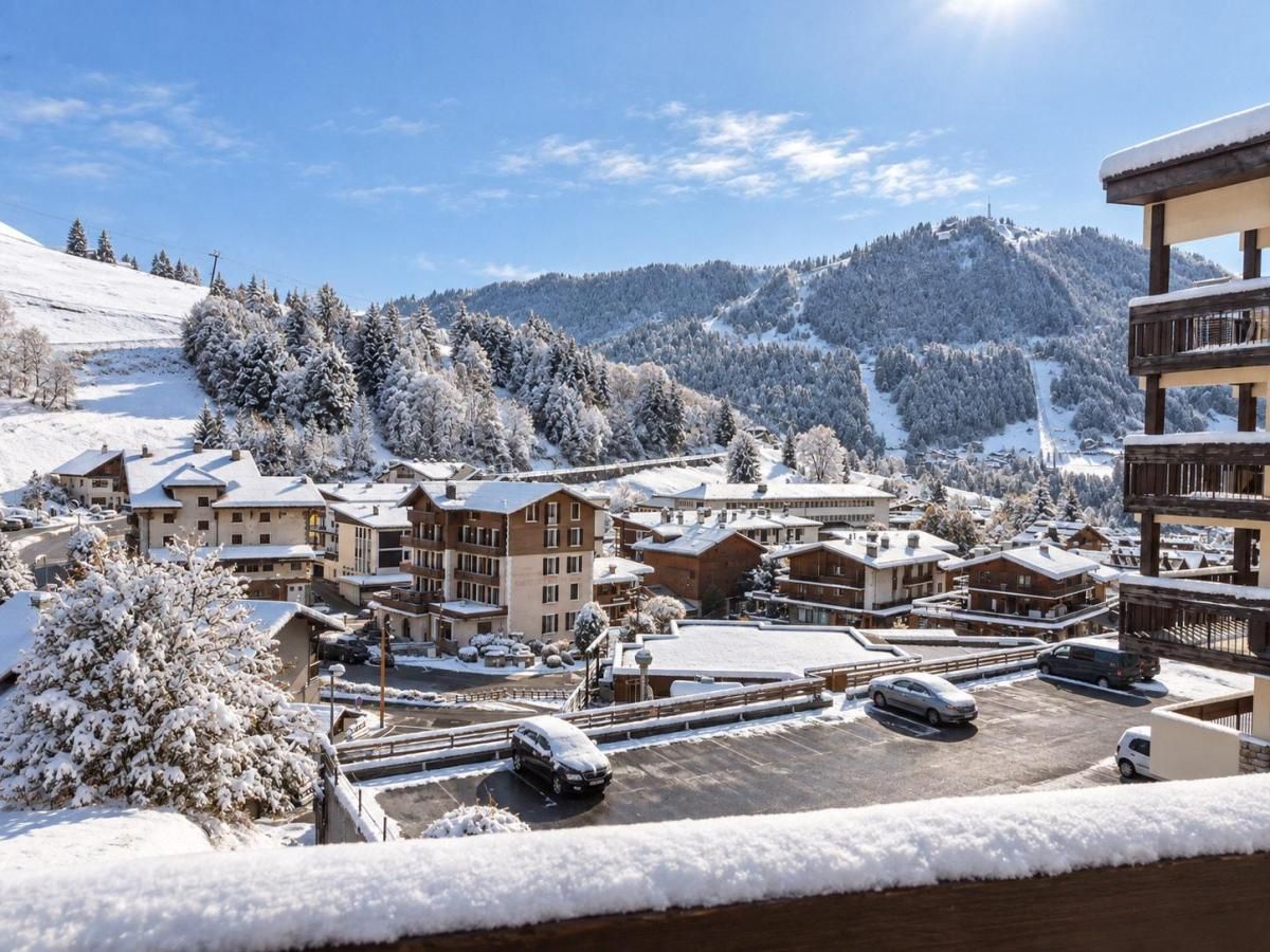 Une station de ski enneigée, composée de plusieurs bâtiments, avec un parking et un paysage montagneux en toile de fond.