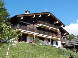 A multi-story chalet with balconies, a wooden facade, and a sloped roof.