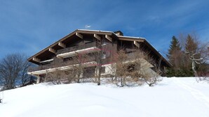 A large wooden chalet with multiple balconies and a sloped roof, surrounded by snow and trees. - 1st floor, view mountain, balcony, tv, ski locker, 37m², La Clusaz (La Clusaz)