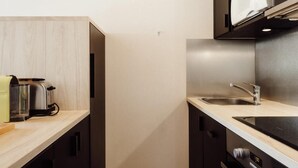 A compact kitchen with dark cabinetry, a wooden ceiling, and a built-in microwave.