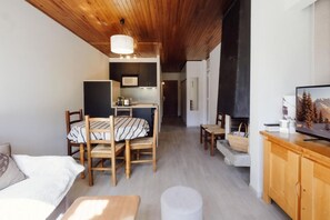 Ein gemütliches Wohnzimmer mit Holzboden, einem Essbereich mit gestreiftem Tischlein und einem Fernseher auf einem Holzschrank.