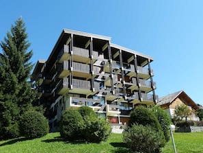 Ein mehrstöckiges Gebäude mit Balkonen, umgeben von Grünflächen und blauem Himmel.