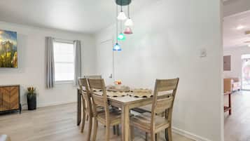 A dining area with a wooden table and chairs, a ceiling light fixture, and a painting on the wall.