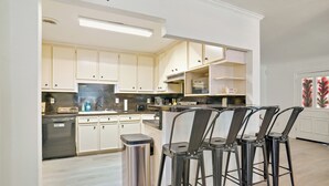 Une cuisine moderne avec des meubles de couleur claire, un lave-vaisselle en acier inoxydable et un coin bar avec des tabourets.