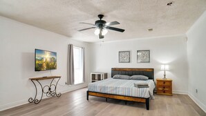 Une chambre à coucher avec un lit, un ventilateur de plafond, une télévision et une fenêtre.