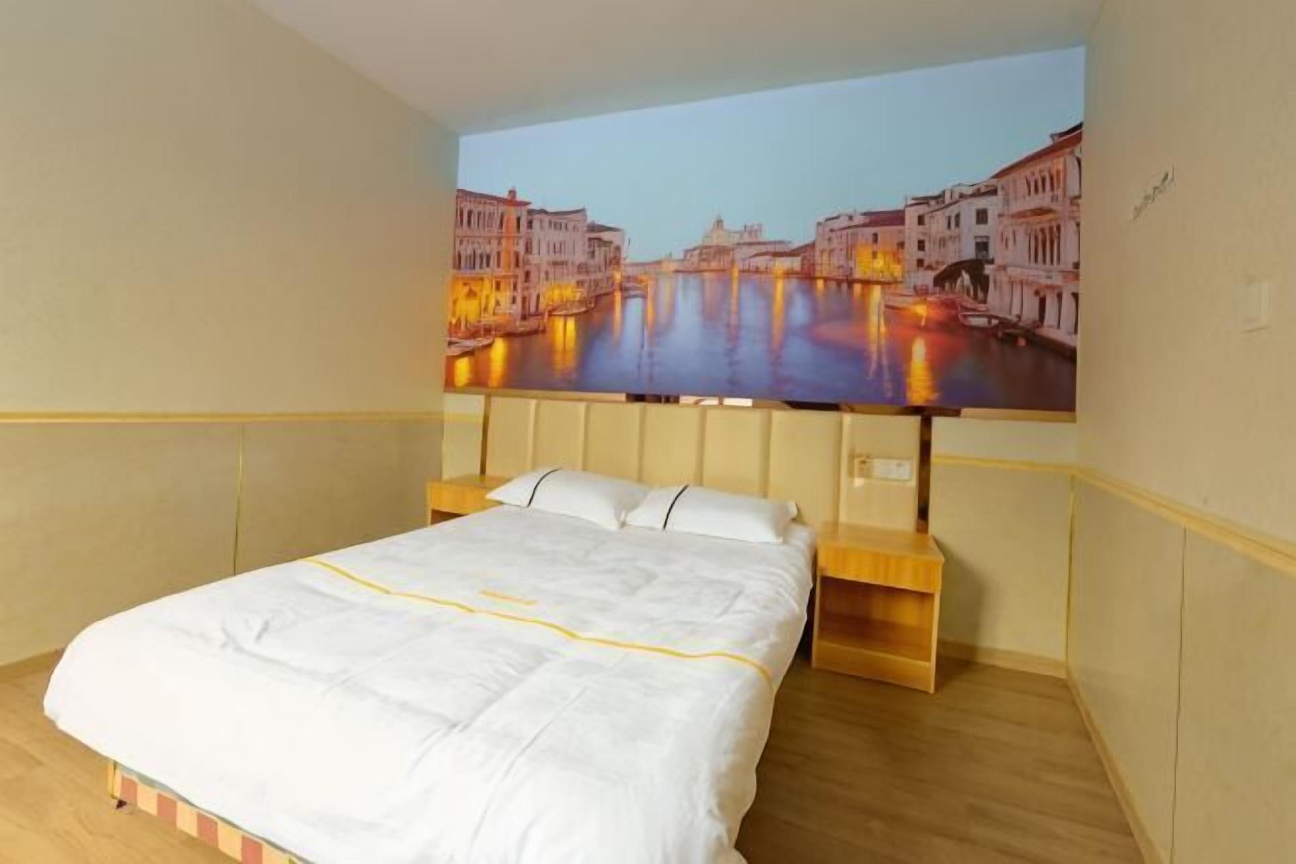 Ein Hotelzimmer mit einem Bett, einem Kopfteil mit einem Stadtbild und einem Nachttisch aus Holz.