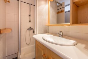 A bathroom with a white sink, wooden cabinets, a mirror, and a shower. - 70m from ski slopes, Ground floor, balcony, tv, 43m², La Clusaz (La Clusaz)
