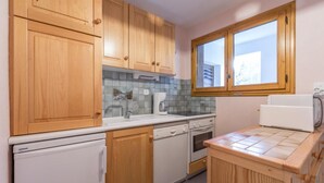 A compact kitchen with wooden cabinets, a built-in dishwasher, an oven, and a window above the sink.