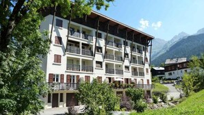 A multi-story hotel with balconies, surrounded by greenery and mountains.