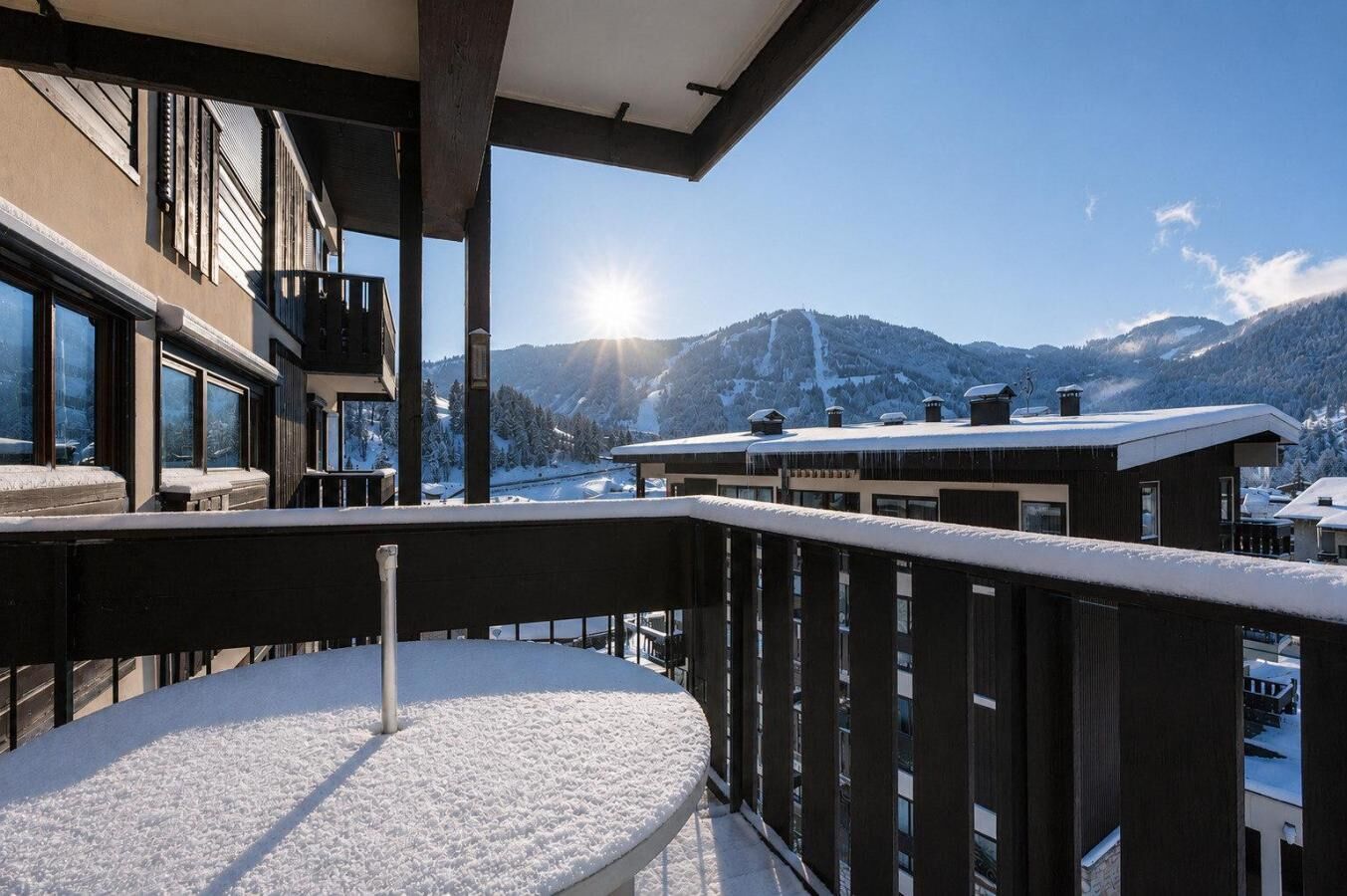 A balcony with a view of snow-covered mountains and a ski slope.