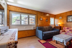 A cozy room with wooden walls, a sofa, a table, and a window with a view of buildings.