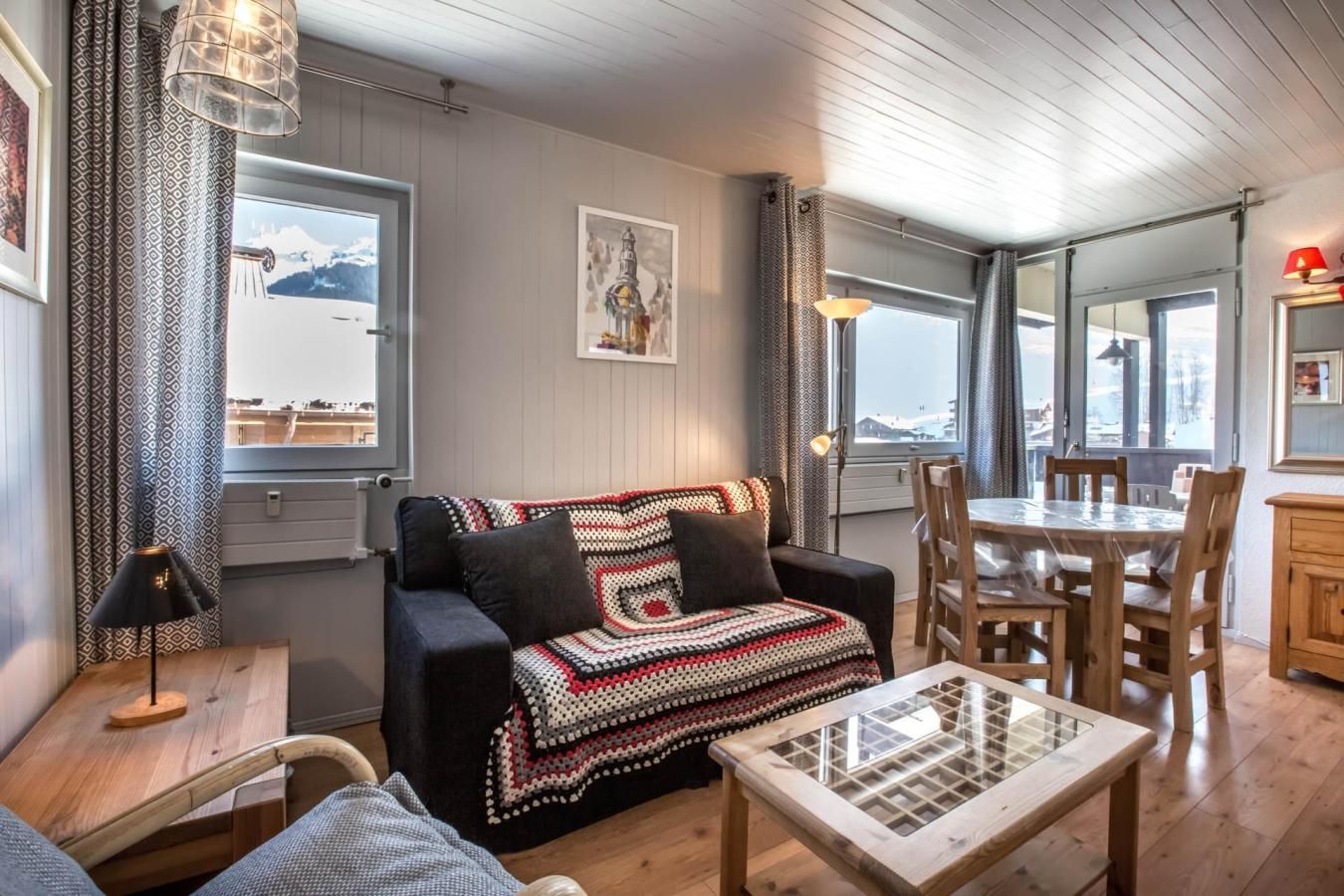 A cozy living room with a black sofa, a glass coffee table, and a dining area with wooden chairs and a table.