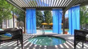 Área de piscina descoberta coberta, com duas cadeiras de vime e uma banheira de hidromassagem.