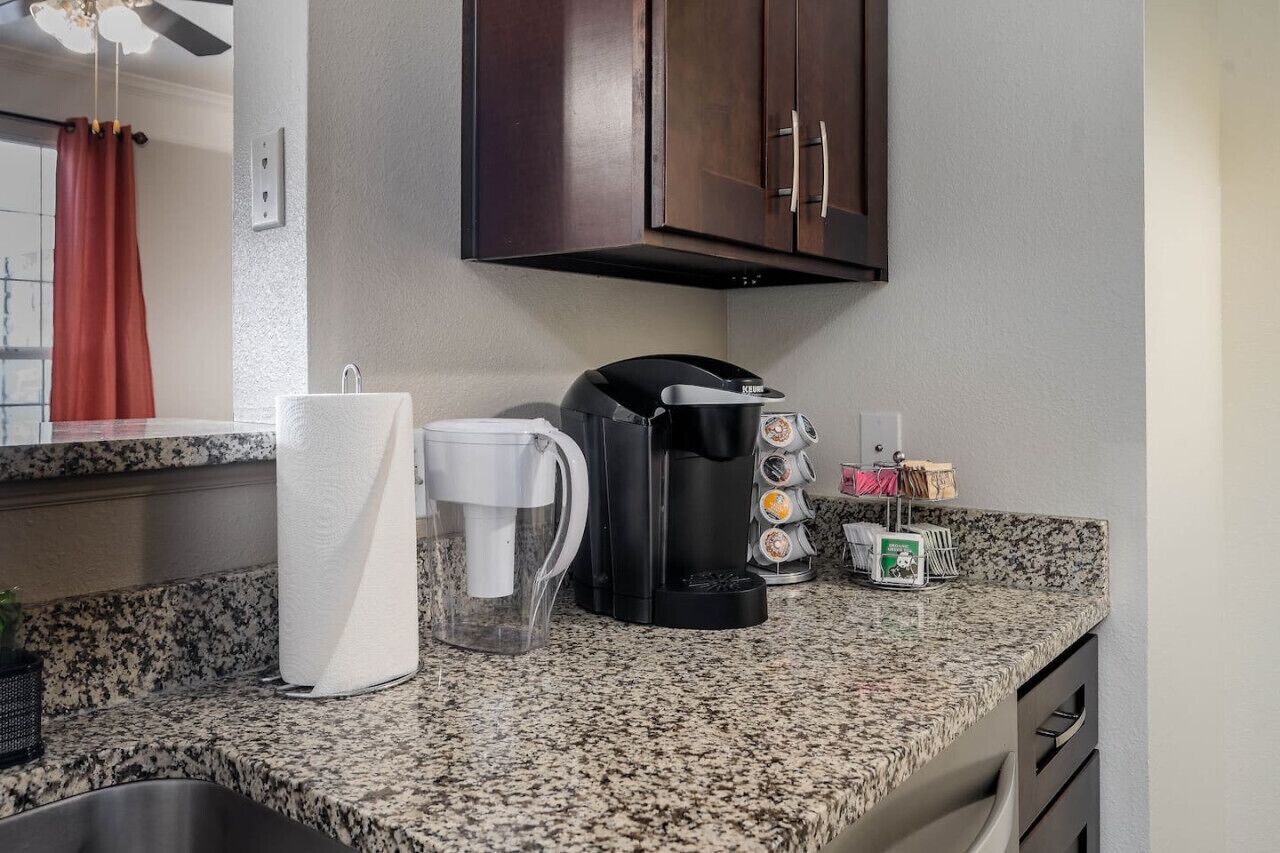 A kitchen with a coffee maker, paper towels, and a coffee pot on the counter.