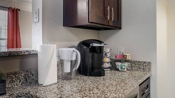 A kitchen with a coffee maker, paper towels, and a coffee pot on the counter.