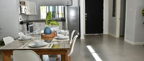 A modern kitchen with white cabinets, a stainless steel refrigerator, and a dining area with a glass table and white chairs.