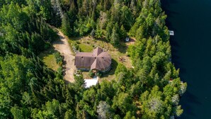An aerial view of a house surrounded by dense forest, with a dock extending into a body of water. - Zulu Zen waterfront cottage (Blue Sea)