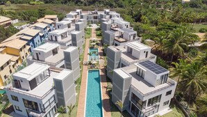 A modern resort with a central pool, multiple buildings, and surrounding greenery.