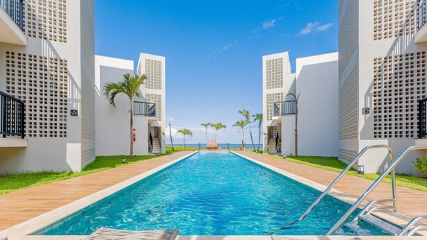 A swimming pool with lounge chairs, palm trees, and a view of the ocean.