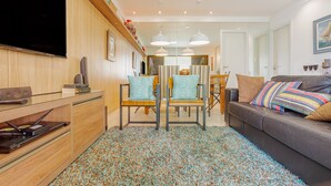 A modern living room with a flat-screen TV, wooden furniture, a patterned rug, and a leather sofa.