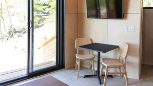 A room with a large window, a flat-screen TV mounted on the wall, two wicker chairs, and a small table. - Cliffside A-Frame (Two Harbors)