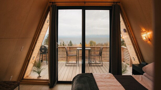 A bedroom with a large window, a bed, and a view of the outdoors. - Cliffside A-Frame (Two Harbors)
