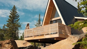 A modern wooden cabin with a sloped roof, a wooden deck, and a view of the surrounding forest. - Cliffside A-Frame (Two Harbors)