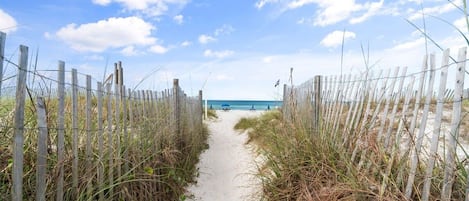 A sandy path leading to a beach with a wooden fence on either side.