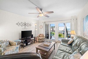 A living room with a television, sofa, and a ceiling fan. - 3BR Sleeps 8 | Sugar Beach | Steps to Beach & Pool (Panama City Beach)