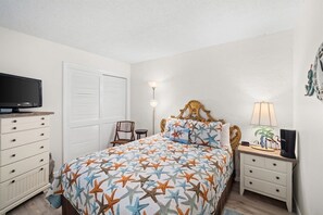 Une chambre à coucher avec un lit, une télévision, une table de chevet, une lampe et une chaise.