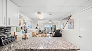 A kitchen with granite countertops, white cabinets, and a toaster. There is a dining area with a table and chairs, and artwork on the walls. - 3BR Sleeps 8 | Sugar Beach | Steps to Beach & Pool (Panama City Beach)