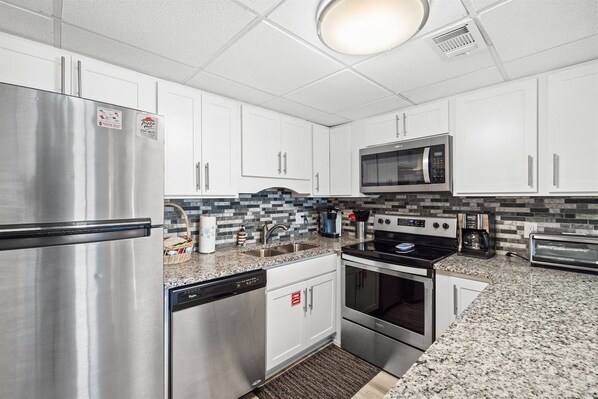 A modern kitchen with stainless steel appliances, white cabinets, and a patterned backsplash.