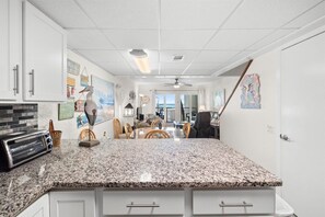 A kitchen with a granite countertop, white cabinets, and a toaster. There is a dining area with chairs and a table.