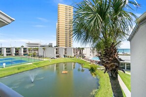 A courtyard with a pool, palm tree, tennis court, and high-rise buildings in the background. - 3BR Sleeps 8 | Sugar Beach | Steps to Beach & Pool (Panama City Beach)